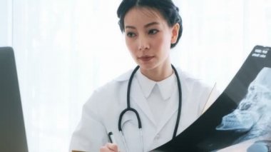 Onun masasında oturan genç Asyalı kadın tıp doktoru hasta xray ve notlar okuma inceleyin. Genç tıp doktoru kariyer kavramı. 