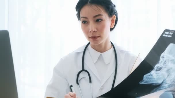 年轻的亚洲女医生坐在她的办公桌上 检查病人的 光和阅读笔记 年轻的医生职业理念 — 图库视频影像