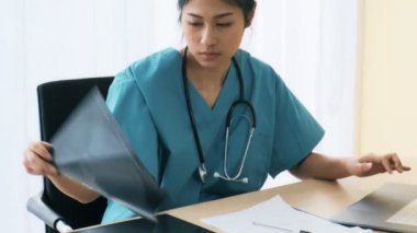 Onun masasında oturan genç Asyalı kadın tıp doktoru hasta xray inceleyin. Genç tıp doktoru kariyer kavramı.