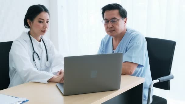 有病人的医生年轻的女医生在医院与一名资深患者交谈 看着她的笔记本电脑讨论体检结果 老年医疗和保险概念 — 图库视频影像