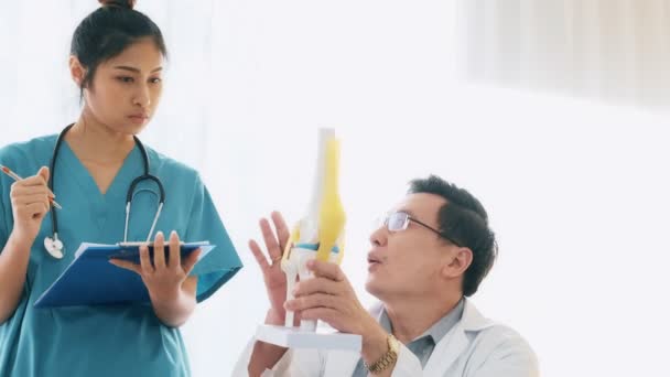 シニア男性医師彼の机の上に座っている若い医療女性医師に話して骨モックアップ ノートを取ることを確認します 若い医師のキャリア概念 — ストック動画