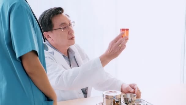 シニア男性医師彼の机の上に座って若い医療女性医師医療薬を保持する話 若い医師のキャリア概念 — ストック動画
