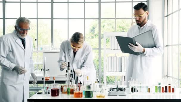 化学実験室での作業のグループ 若者は白いノート白人化学研究室で一緒に作業をシニアと男性と女性の化学者です 科学のコンセプト — ストック動画