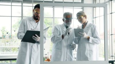 Bir laboratuarda çalışan kimyagerler grubudur. Genç erkek ve dişi kimyagerler cam ekran üzerinde yazma birlikte laboratuarda, çalışan üst düzey beyaz kimyager ile beyaz. Bilim kavramı.