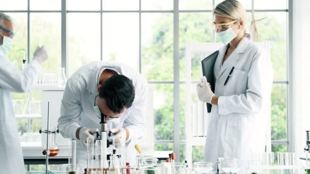 化学実験室での作業のグループ 若い白顕微鏡に見て白人化学研究室で一緒に作業をシニアと男性と女性の化学者 科学のコンセプト — ストック動画