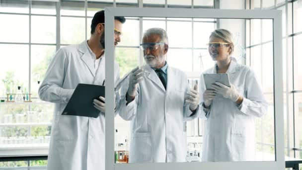 在实验室工作的化学家小组 年轻的白人男女化学家与高级高加索化学家一起在实验室工作 在玻璃显示屏上写作 科学理念 — 图库视频影像