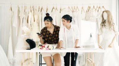 Birlikte çalışan genç moda evi tasarımcı. Bir gelinliğin genç Asyalı kadın ile müşteriler emir alan bilgisayar hem de telefonda. Küçük işletme kavramı.