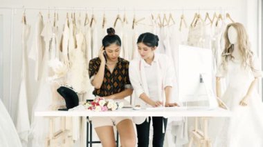 Birlikte çalışan genç moda evi tasarımcı. Bir gelinliğin genç Asyalı kadın ile müşteriler emir alan bilgisayar hem de telefonda. Küçük işletme kavramı.