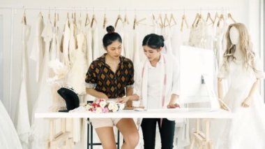 Birlikte çalışan genç moda evi tasarımcı. Bir gelinliğin genç Asyalı kadın ile müşteriler emir alan bilgisayar hem de telefonda. Küçük işletme kavramı.