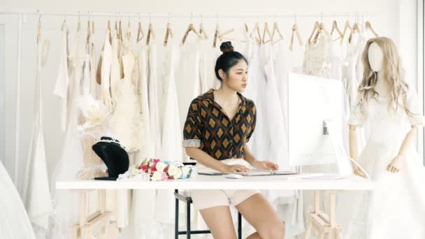 若者のファッションの家デザイナー ブライダル ドレス 顧客の注文を取って コンピューターとの若いアジアの女性 スモール ビジネス コンセプト — ストック動画