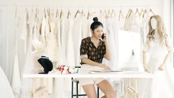 若者のファッションの家デザイナー ブライダル ドレス 若いアジア女性コンピューターと電話で話し 顧客注文を取っています スモール ビジネス コンセプト — ストック動画