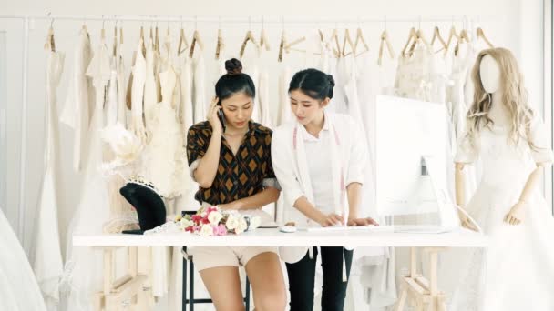 若者のファッション家のデザイナーが一緒に働きます ブライダル ドレス 若いアジア女性顧客に注文を取って コンピューターと電話 スモール ビジネス コンセプト — ストック動画