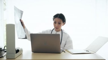 Onun masasında oturan genç Asyalı kadın tıp doktoru hasta tıbbi profili inceleyin. Genç tıp doktoru kariyer kavramı.