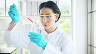 Asya kimyager bir laboratuarda çalışan. Genç kadın kimyager kimyasal sıvı test tüpü içinde koyarak atış kapatın. Bilim kavramı.