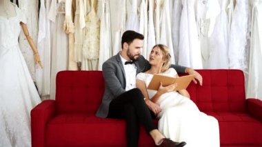 Romantik düğün çift pahalı kıyafet Dükkanı. Beyaz adam ve kadın gelin elbise, birlikte kitaba bakmalısın kanepede oturuyor. Romantik genç çift kavramı.