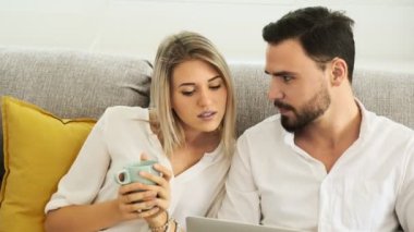 Young couple working together at home on sofa using laptop, discussing work. White man and woman. Freelance concept.\