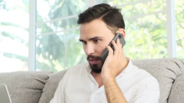 Onun dizüstü bilgisayarda çalışan ve müşteri için telefonda konuşurken kanepede oturan genç adam. Sakal, freelence kavramı ile beyaz erkek.