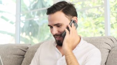 Onun dizüstü bilgisayarda çalışan ve müşteri için telefonda konuşurken kanepede oturan genç adam. Sakal, freelence kavramı ile beyaz erkek.