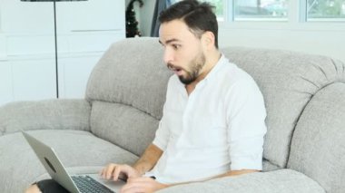 Genç onun laptop çalışma kanepede oturan adam ve bir sürpriz ile iyi haber bulundu. Sakal, freelence kavramı ile beyaz erkek.