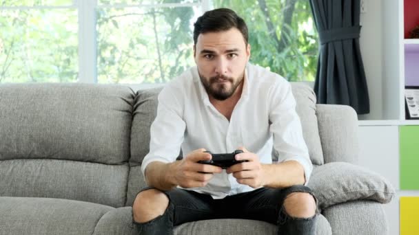 若い男がカメラの前でコンソールゲームをプレイし 彼の対戦相手をオンラインで打ちます ソファの上の白人 Eスポーツ競技の概念 — ストック動画