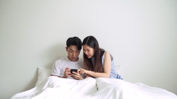 一对躺在床上的夫妇以获胜的姿势看着手机 亚洲人中国男人和女人在床上的白天与笔记本电脑 现代生活方式理念 — 图库视频影像