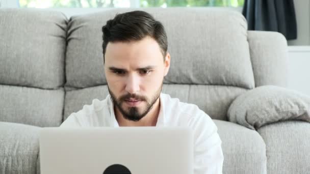 坐在地板上的年轻人在笔记本电脑上工作 对着镜头微笑 有胡子的白男 自由快乐的生活方式概念 — 图库视频影像