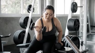 Genç Asyalı kadın spor salonunda dambılı kaldırmaya çalışıyor. Otantik Fitness yaşam tarzı konsepti.