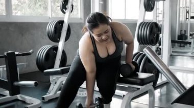 Genç Asyalı kadın spor salonunda dambılı kaldırmaya çalışıyor. Otantik Fitness yaşam tarzı konsepti.