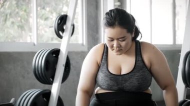 Genç şişman Asyalı kadın spor salonundaki yoğun eğitimden sonra yedek kulübesinde dinleniyor. Otantik Fitness yaşam tarzı konsepti.