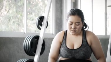 Genç şişman Asyalı kadın spor salonundaki yoğun eğitimden sonra yedek kulübesinde dinleniyor. Otantik Fitness yaşam tarzı konsepti.