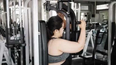 Genç şişman Asyalı kadın jimnastik salonunda göğüs güvertesi makinesini kullanmaya çalışıyor. Otantik Fitness yaşam tarzı konsepti.