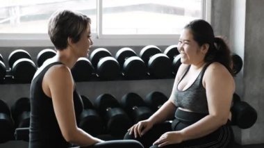 Genç ve cüsseli Asyalı kadın beyaz antrenörüyle oturup kilo verme hedefleri hakkında konuşuyor. Otantik Fitness yaşam tarzı konsepti.