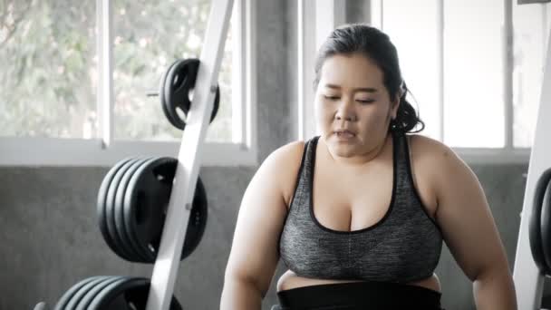 ジムでの集中トレーニングコースの後 若い脂肪アジアの女性がベンチで休んでいます 本物のフィットネスライフスタイルコンセプト — ストック動画