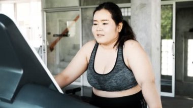 Genç ve şişman Asyalı kadın koşu bandında dinleniyor. Otantik fitness yaşam tarzı.