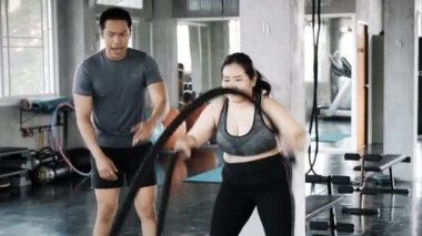 Genç adam büyük beden öğrencisine savaş halatını nasıl kullanacağını öğretmeye çalışıyor. Otantik fitness yaşam tarzı.