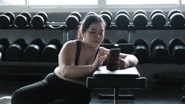 Asyalı artı boyutu kadın telefonda arkadaşı yla sohbet spor salonunda katta istirahat.