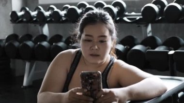 Asyalı artı boyutu kadın telefonda arkadaşı yla sohbet spor salonunda katta istirahat.