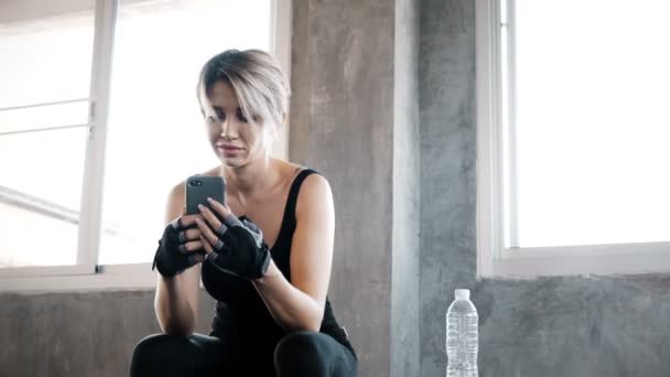 正宗的年轻白人妇女使用她的手机在健身房记录和聊天与她的朋友 而休息 健身移动技术概念 — 图库视频影像