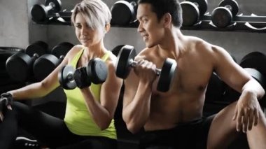 Genç, sarışın, beyaz kadın, spor salonunda Asyalı bir adamla birlikte halteri kaldırıyor. Otantik fitness yaşam tarzı. 