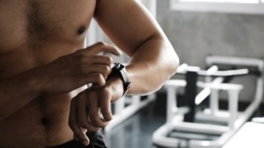 Genç Asyalı bir adam spor salonunda akıllı bir saat kullanıyor. Asyalı adam ayağa kalktı, saatine dokundu.. 