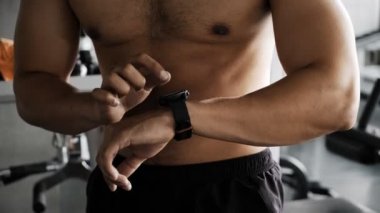 Genç Asyalı bir adam spor salonunda akıllı bir saat kullanıyor. Asyalı adam ayağa kalktı, saatine dokundu.. 