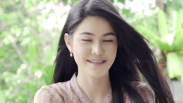 超级慢动作的年轻美丽的亚洲女人看着和微笑的相机在她的家庭花园与绿色树的背景 特写镜头 千禧年生活方式概念 — 图库视频影像