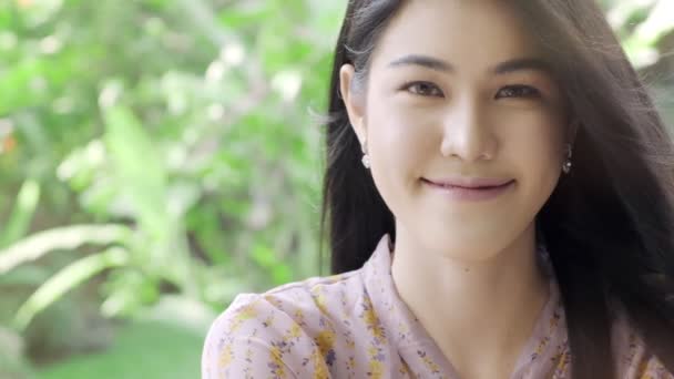 ミレニアル世代のアジアの女性のスーパースローモーションは コピースペースと背景に緑の木と彼女の家の庭でカメラの肖像画に笑顔 ミレニアルライフスタイルコンセプト — ストック動画