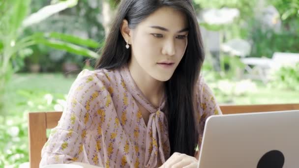 年轻迷人的亚洲女人在自家花园的笔记本电脑上工作 背景是绿树 专注于工作 近距离拍摄 千年自由职业者生活方式概念 — 图库视频影像