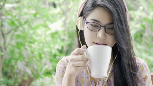 年轻迷人的亚裔女学生 听着音乐 看着笔记本电脑 喝着背景绿树成荫的咖啡 千年教育生活方式概念 — 图库视频影像