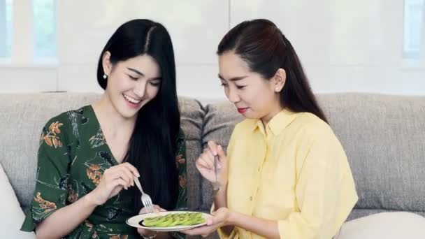 若い美しいアジアの女性はソファの上で母親のキウイを食べ 彼女をからかい 楽しんでいます 若い女性関係の概念 — ストック動画