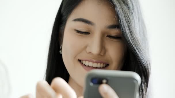 年轻美丽的亚洲女人坐在卧室的床上 一边看手机 一边笑着 走近镜头 青少年社交媒体参与生活方式概念 — 图库视频影像