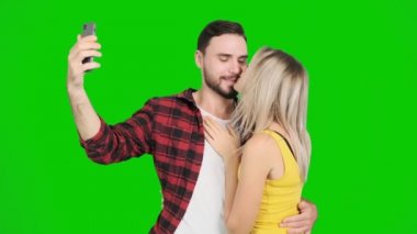 Genç adam yeşil ekranda bir kadınla selfie çekiyor. Beyaz erkek ve kadın, krom anahtar..