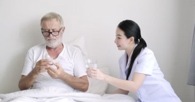 Genç asyalı hemşire kıdemli hastaya su ile hap veriyor