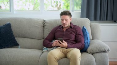 Kafkas eşcinsel adam kanepede oturuyor ve evde cep telefonu kullanıyor